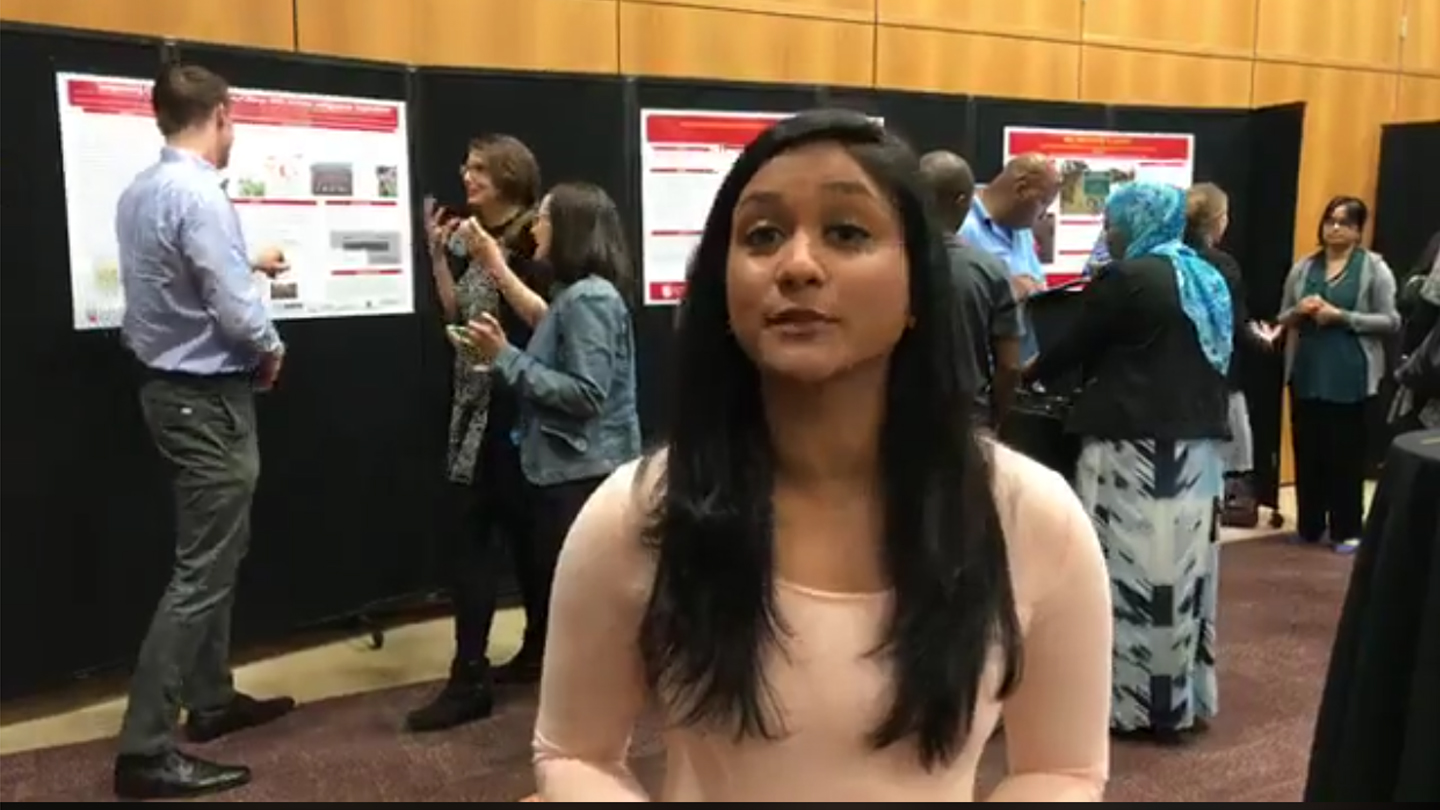 2017 Graduate Student Symposium, student host introduces event, posters behind her