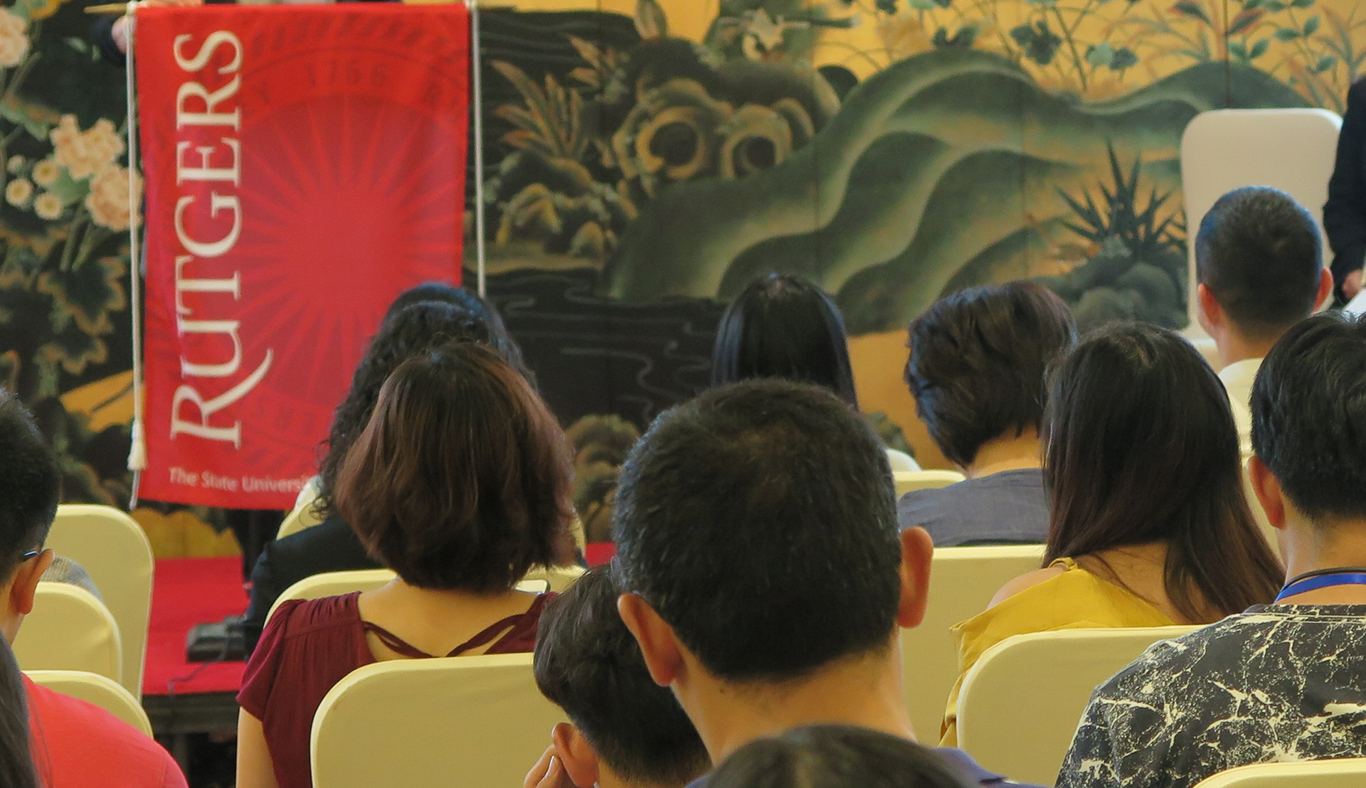 Rutgers Global - Rutgers Hosts First Pre-Departure Orientation in China for U.S.-Bound Undergraduate Chinese Students, student attendees look on to a stage where a podium with a Rutgers drape is positioned