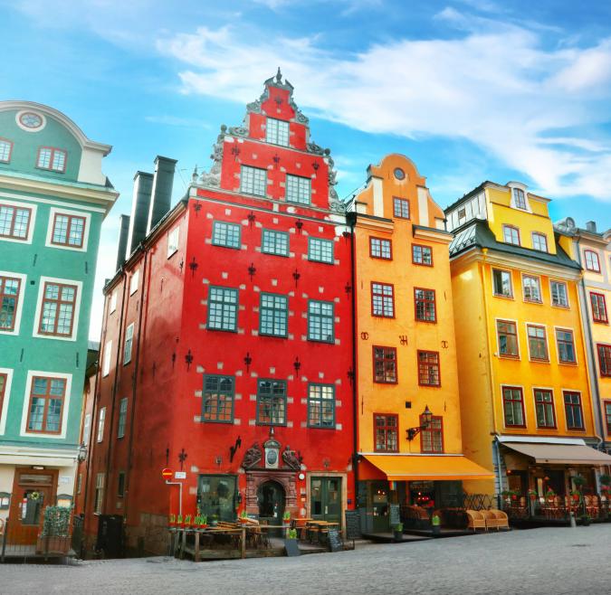 A row of traditional Scandinavian style homes in bright greens, oranges, and yellows are pictured on a hill on a sunny day