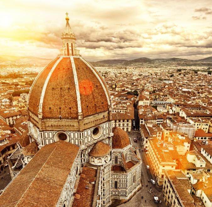 Birds eye view of the Florence Duomo. The sign is shining over the city and there is a mountain in the background.