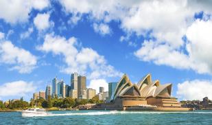 Viewed from the harbor, Sydney Opera House is pictured in the center with it's famous seashell shape and the skyline is visible in the background