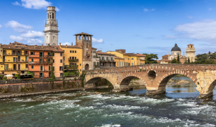 Scenic view of Verona's Ponte Pietra and historic buildings under a blue sky.