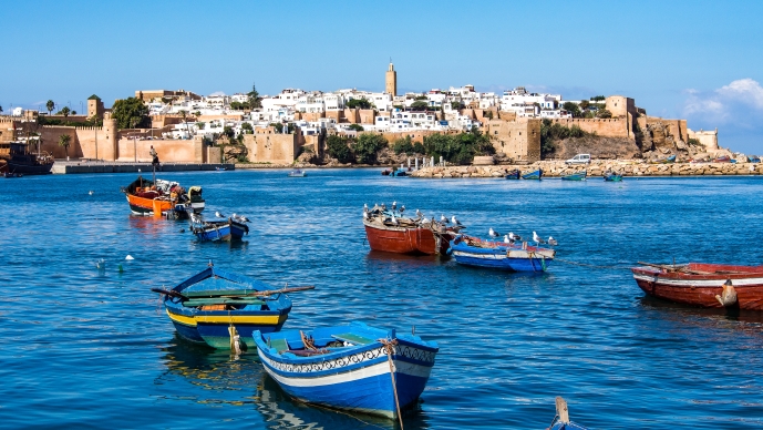 Colorful boats sit on the blue ocean water with a seaside town in the background