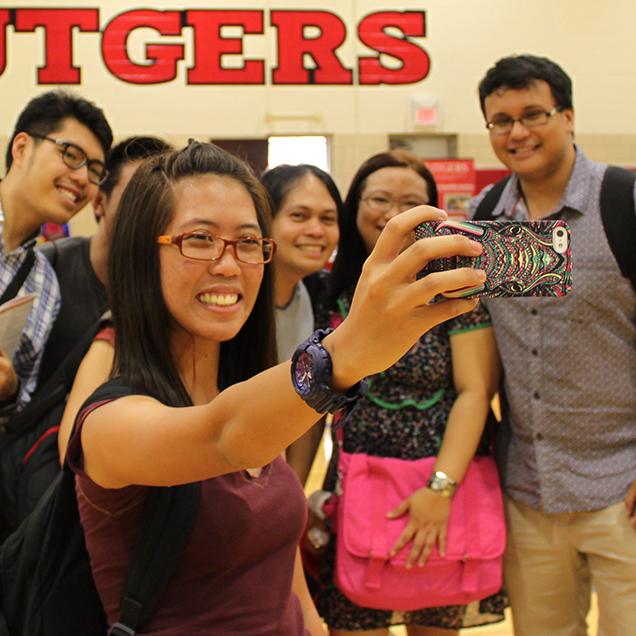 Rutgers Global – Tailored Group or Certificate Programs, six students pose for a group selfie in Rutgers gym, girl holds a multicolored phone