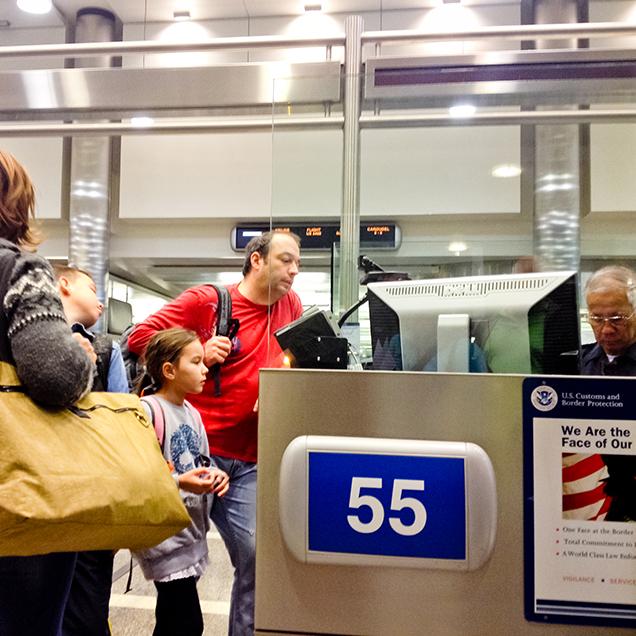 Rutgers Global - Requesting J-2 Documents for Dependents of Scholars and Research Students, a man, his wide, and young daughter speak with an older customs agent at an airport before entering the U.S. 