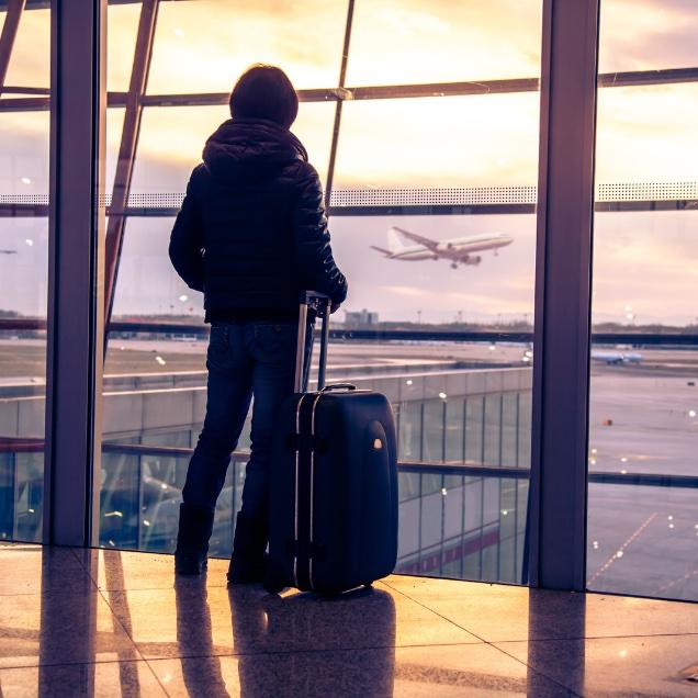 Person at airport looking out window at plane taking off